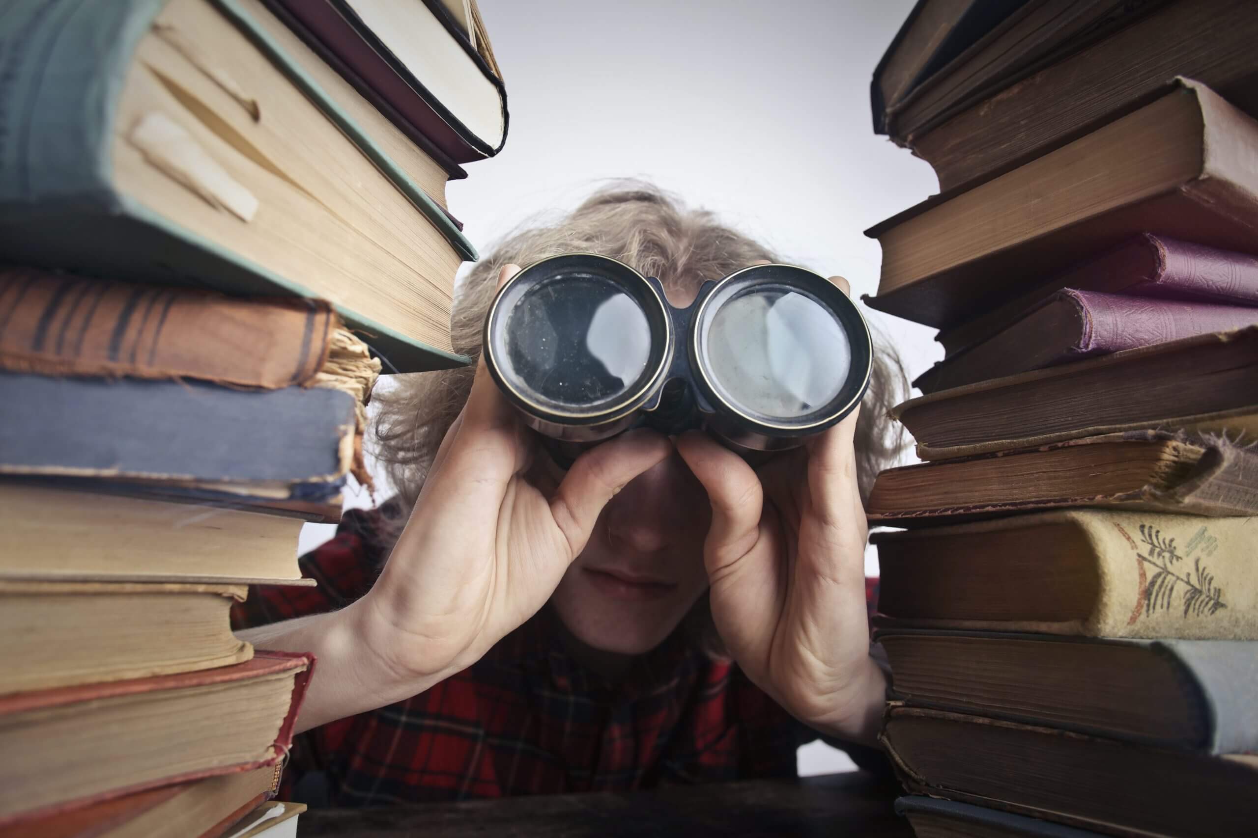 homme entre deux piles de livres avec des jumelles